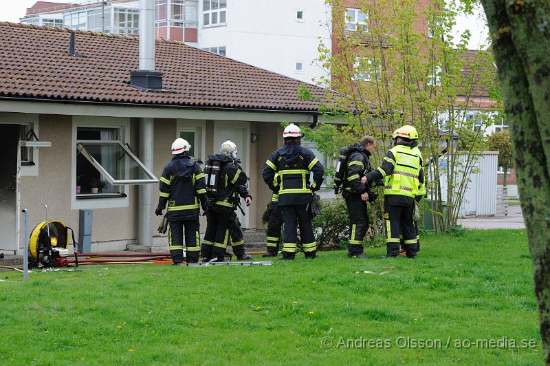 _DSC8266.JPG - Vid 10.40 larmades en större räddningsstyrka med räddningstjänsten från Åstorp, Klippan, Helsingborg samt polis och ambulans till ett radhus på hantverkargatan i Åstorp där man fått in larm om brand i en av lägenheterna. På plats konstaterade räddningstjänsten från åstorp att det var en fullt utvecklad brand i lägenheten men man fick snabbt kontroll över branden men hela lägenheten skadades. Ingen person ska ha kommit till skada men tyvärr avled en hund i branden. Enligt vittne på plats hade man sett en kvinna kasta in något genom fönstret strax innan branden började. Polisen rubricerar händelsen som grov mordbrand.