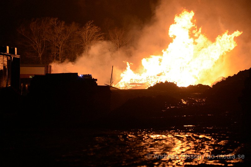 DSC_7888.JPG - Vid 21.40 larmades räddningstjänst, ambulans och polis till Gyllsjö trä i Stidsvig där man hade en fullt utvecklad brand i ett pall lager med ungefär 10 000 trä pallar. Lagret var helt övertänt när räddningstjänsten kom fram till platsen och man inrikta sig direkt på att skydda omkring liggande byggnader. Bland annat produktionslokalen som ligger ungefär 20 meter från pall lagret. Den kraftiga strålnings värmen från branden gjorde att det började brinna lite i fasaden på produktionslokalen men man lyckades begränsa branden och skydda byggnaden. Vid tre tiden på natten fick man en brand uppe i taket på produktionslokalen och man fick sätta in fler resurser, men kallade in en hävare och skickade upp folk på taket för att begränsa branden och kontrollera så den inte kunde sprida sig. Det arbetet gav också snabbt resultat och skadorna blev bregränsade. Ingen person har kommit till skada men lager byggnaden är helt nedbränd och produktionslokalen har fått skador i ena fasaden. Räddningstjänsten hade flera stationer på plats under kvällen/natten, Klippan, Åstorp, Ljungbyhed; Örkelljunga, Ängelholm, Helsingborg.